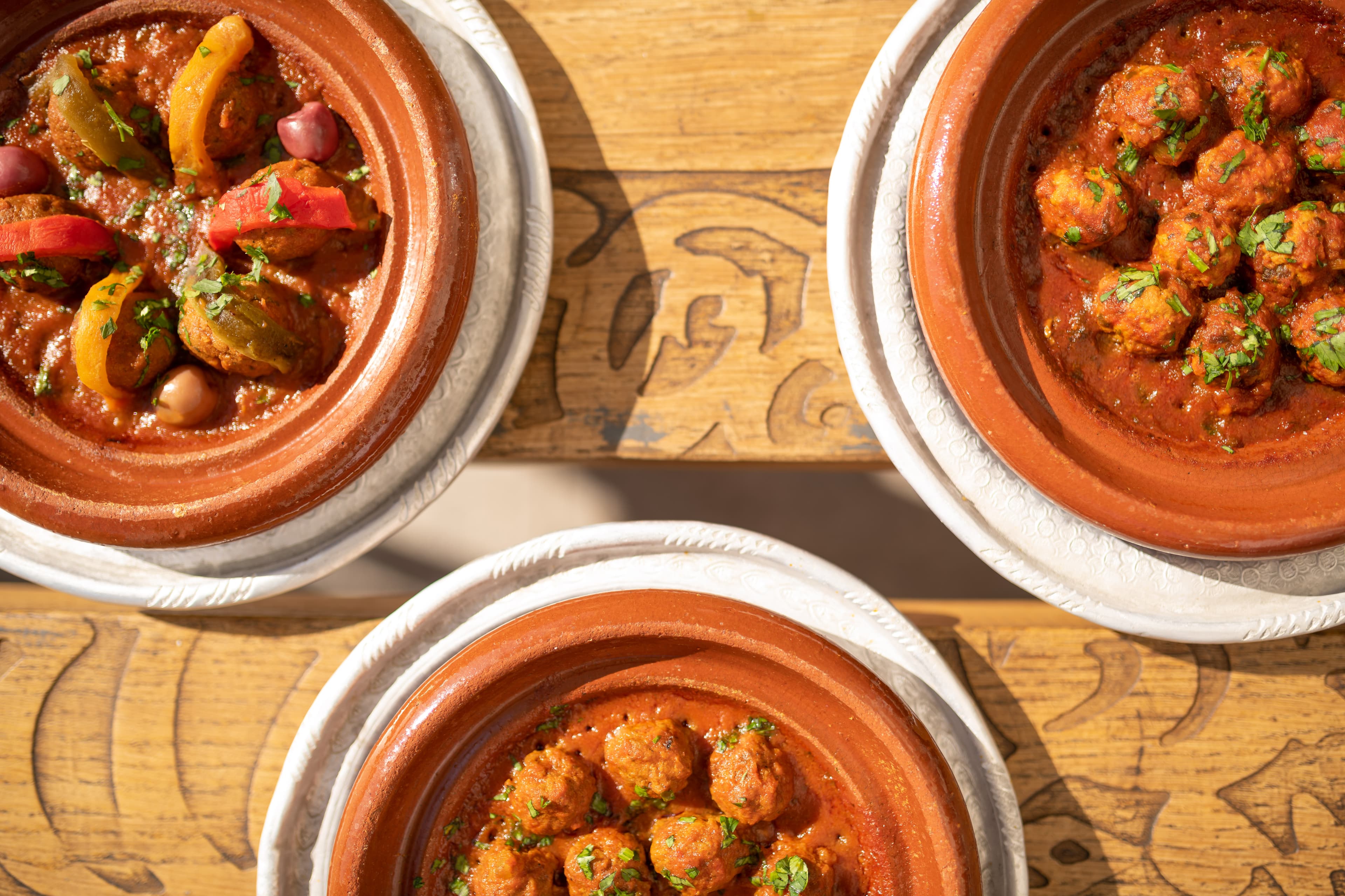 Trois tajines de kefta sur planche en bois sculptée.