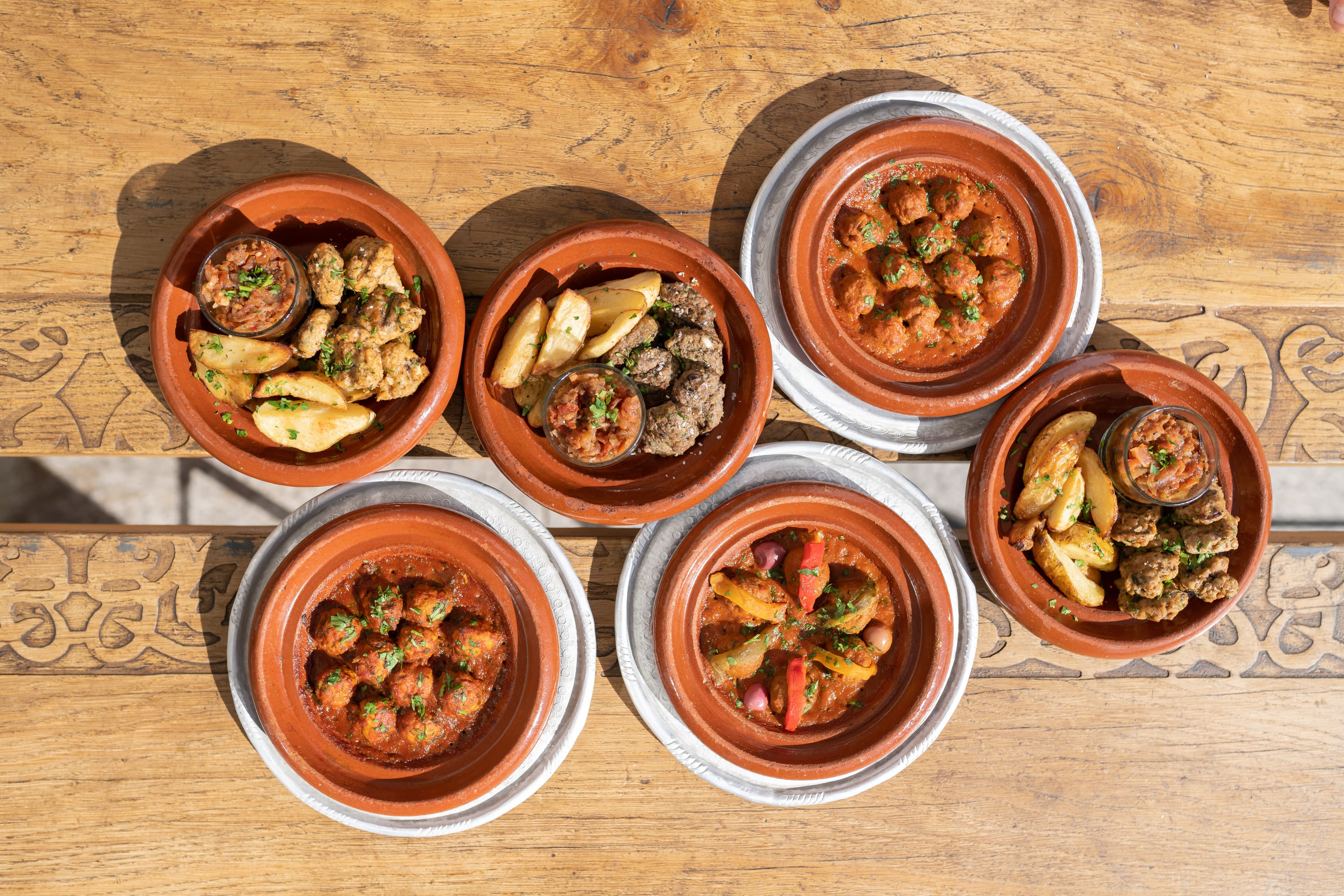 Six mini-tajines en plongée sur une table en bois sculptée, recettes du jour Moojood.