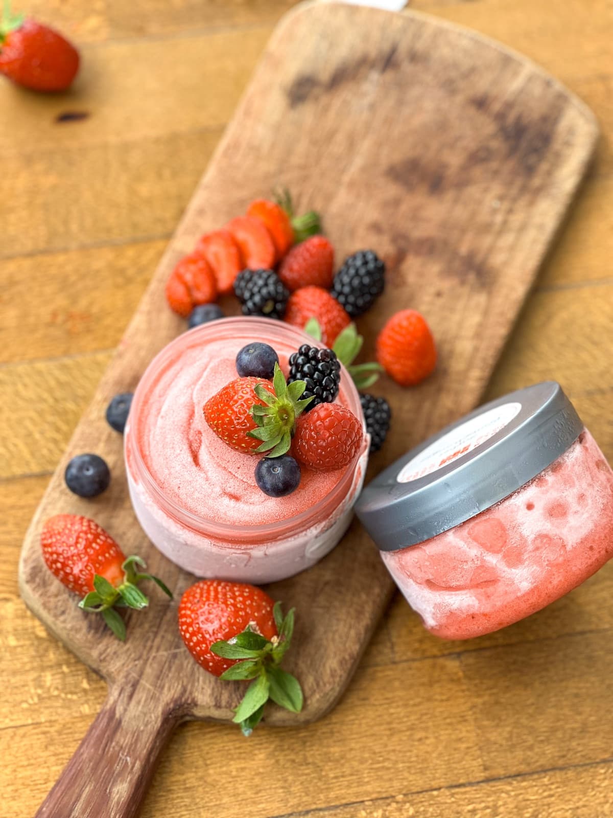 Sorbet fraise Moojood en pot, entouré de fraises et de fruits rouges sur planche en bois.