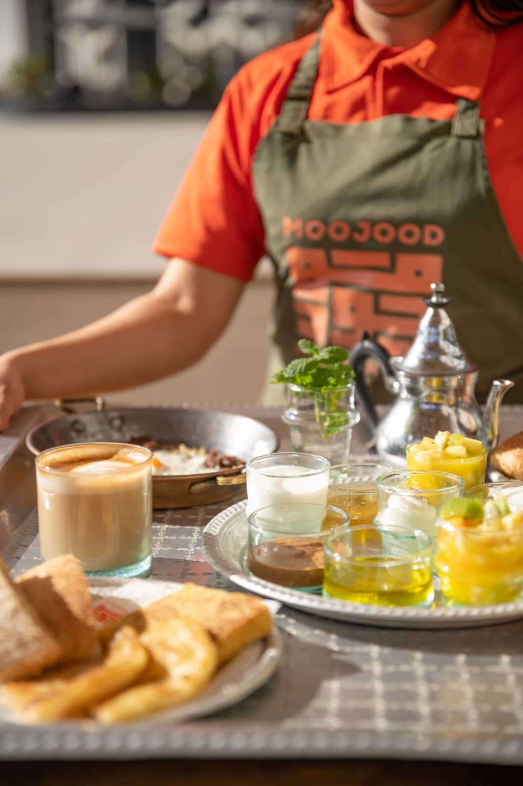 Moojood breakfast tray being served, branded apron in view.
